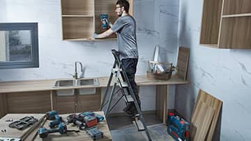 ชายคนหนึ่งกำลังติดตั้งชั้นวางในครัวสมัยใหม่โดยใช้เครื่องมือ Bosch.