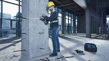 ช่างซ่อมคนหนึ่งที่สวมหมวกกันน็อคสีเหลืองกำลังเจาะเสาคอนกรีต.