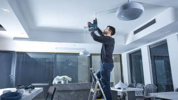 ชายคนหนึ่งกำลังใช้เครื่องมือ Bosch Professional บนบันไดในสำนักงาน.