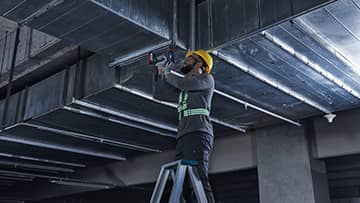 คนงานบนบันไดกำลังติดตั้งชิ้นส่วนโลหะที่เพดาน.