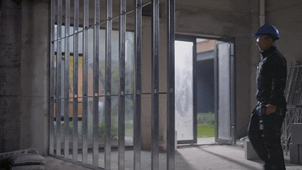 คนงานที่สวมหมวกนิรภัยสีน้ำเงินเดินผ่านโครงสร้างเหล็กที่ยังสร้างไม่เสร็จ.