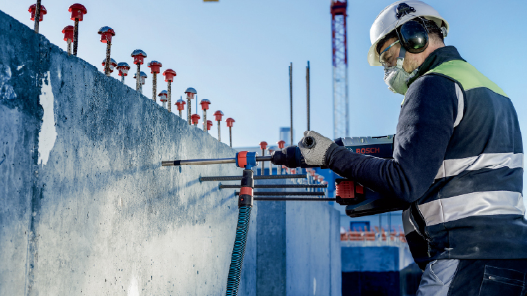 คนงานที่มีเครื่องมือ Bosch กำลังทำงานบนผนังคอนกรีตที่ไซต์ก่อสร้าง.