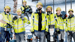 คนงานก่อสร้างหกคนสวมหมวกกันน็อคสีเหลืองและเสื้อกั๊กเตือนภัยยืนอยู่ที่ไซต์ก่อสร้าง.