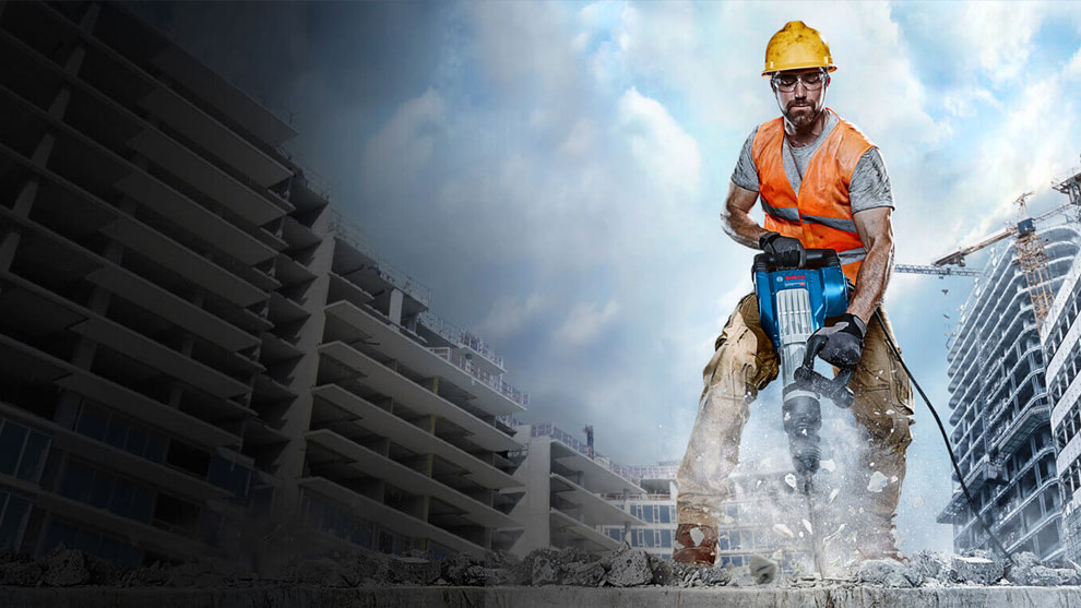 ชายคนหนึ่งสวมหมวกนิรภัยและเสื้อกั๊กสีส้มกำลังทำงานกับค้อน Bosch.