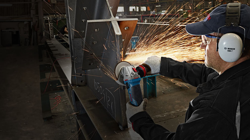 ชายคนหนึ่งกำลังตัดโลหะด้วยเครื่องมือ Bosch สีน้ำเงิน. ประกายไฟกำลังบิน.