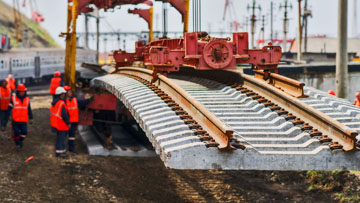 คนงานในชุดสีส้มกำลังวางรางด้วยเครน.