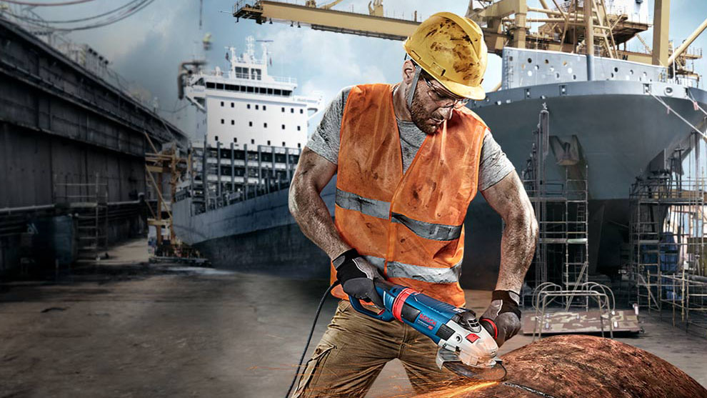 คนงานที่สวมหมวกนิรภัยกำลังตัดโลหะด้วยเครื่อง Bosch สีน้ำเงิน.