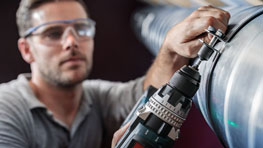 ช่างฝีมือที่สวมแว่นตานิรภัยกำลังใช้งานสว่านสีดำของ Bosch.