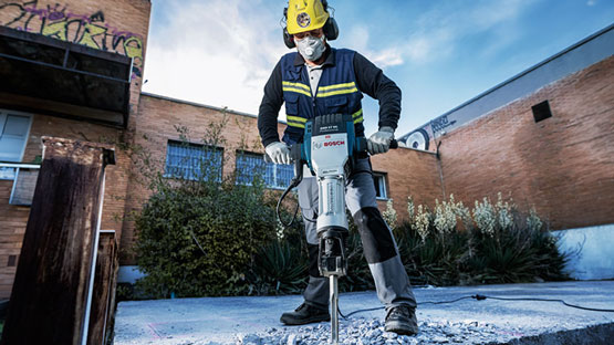 คนงานที่มีค้อน Bosch กำลังทำงานกับคอนกรีตกลางแจ้ง.