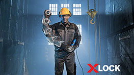 ชายคนหนึ่งสวมหมวกกันน็อคสีเหลืองถือเครื่องมือ Bosch XLOCK ในโรงงาน.