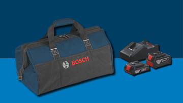 กระเป๋าเครื่องมือสีน้ำเงินของ Bosch ที่มีโลโก้สีแดงวางอยู่บนพื้นหลังสีน้ำเงินข้างๆ กับแบตเตอรี่สองก้อนและที่ชาร์จ.