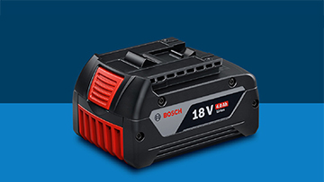 แบตเตอรี่ Bosch Professional 18V สีดำวางอยู่บนพื้นหลังสีน้ำเงิน แบตเตอรี่มีจุดเด่นสีแดงและสีเทา.