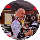 ชายคนหนึ่งสวมหมวกกันน็อคและชุดแข่งยกนิ้วโป้งขึ้นหน้ากระโจมและเครื่องมือ.