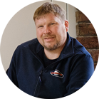 ชายยิ้มที่มีผมสั้นสวมสเวตเตอร์สีน้ำเงิน.