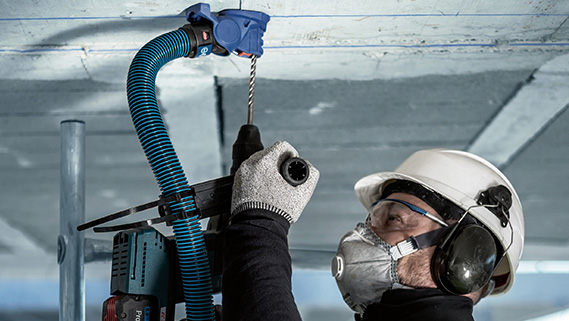 ช่างที่สวมหมวกนิรภัยและที่ป้องกันเสียงกำลังเจาะเพดาน.