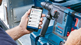 บุคคลหนึ่งกำลังใช้สมาร์ทโฟนข้างเครื่องมือสีน้ำเงิน Bosch Professional.